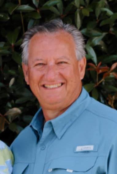 A man with gray hair and blue shirt smiling.
