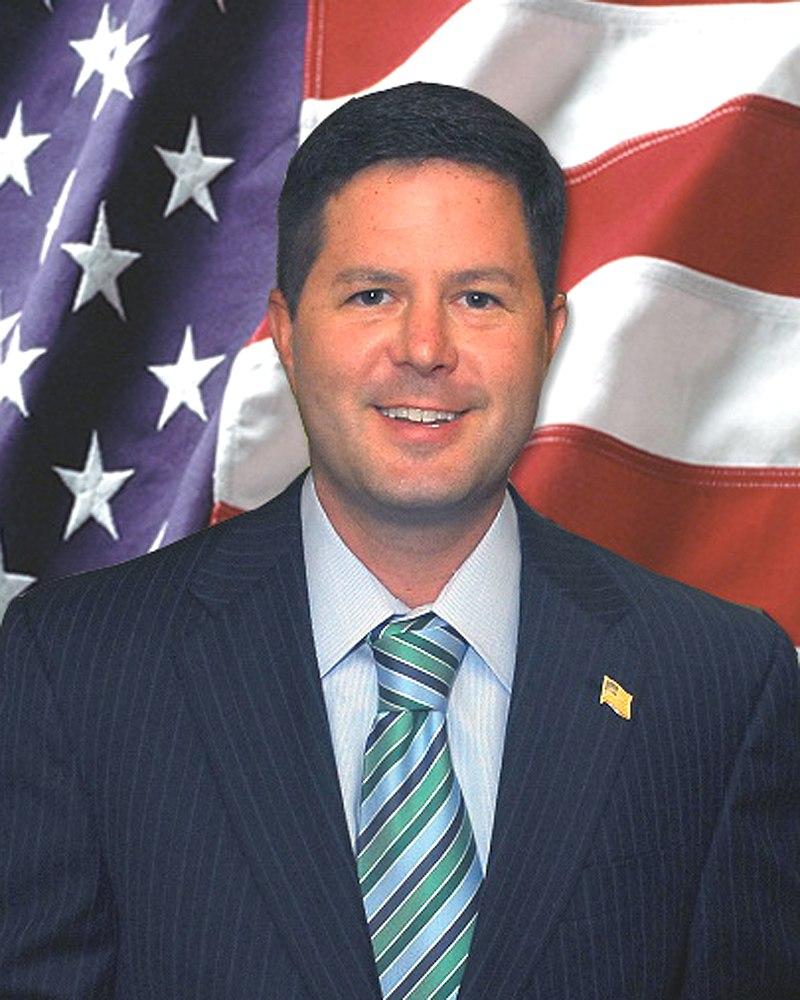 A man in suit and tie standing next to an american flag.