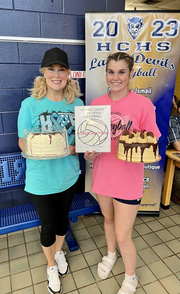 Two women holding cakes and a poster