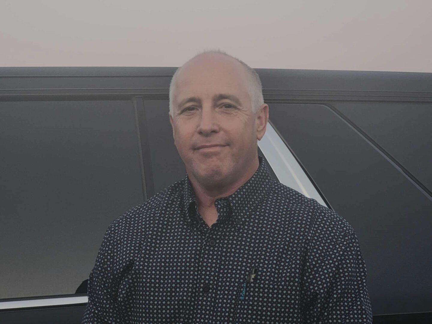 A man in a black shirt is standing next to a car