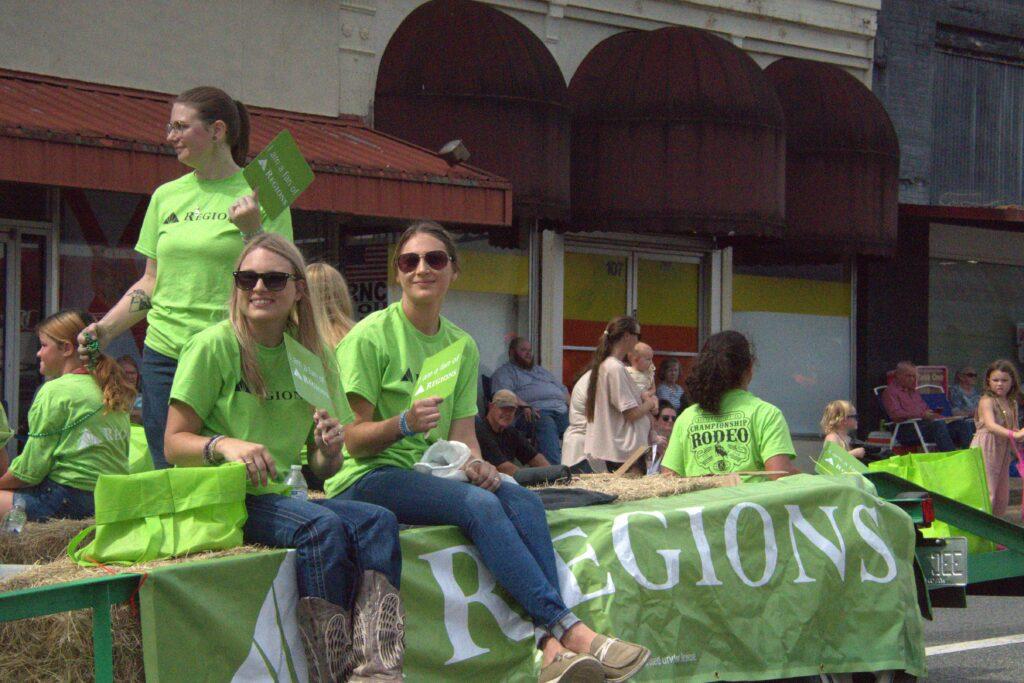 A group of people in green shirts sitting on top of a float.