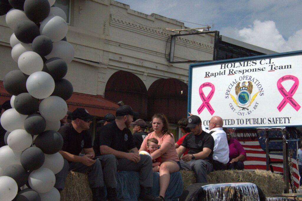 A group of people sitting on hay bales in front of a building.