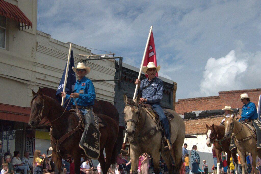 Two men on horses with flags in the back.