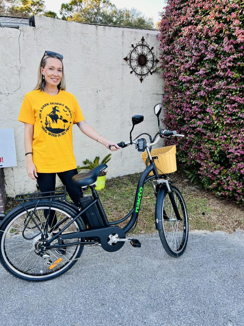 A woman standing next to her bike in front of a wall.