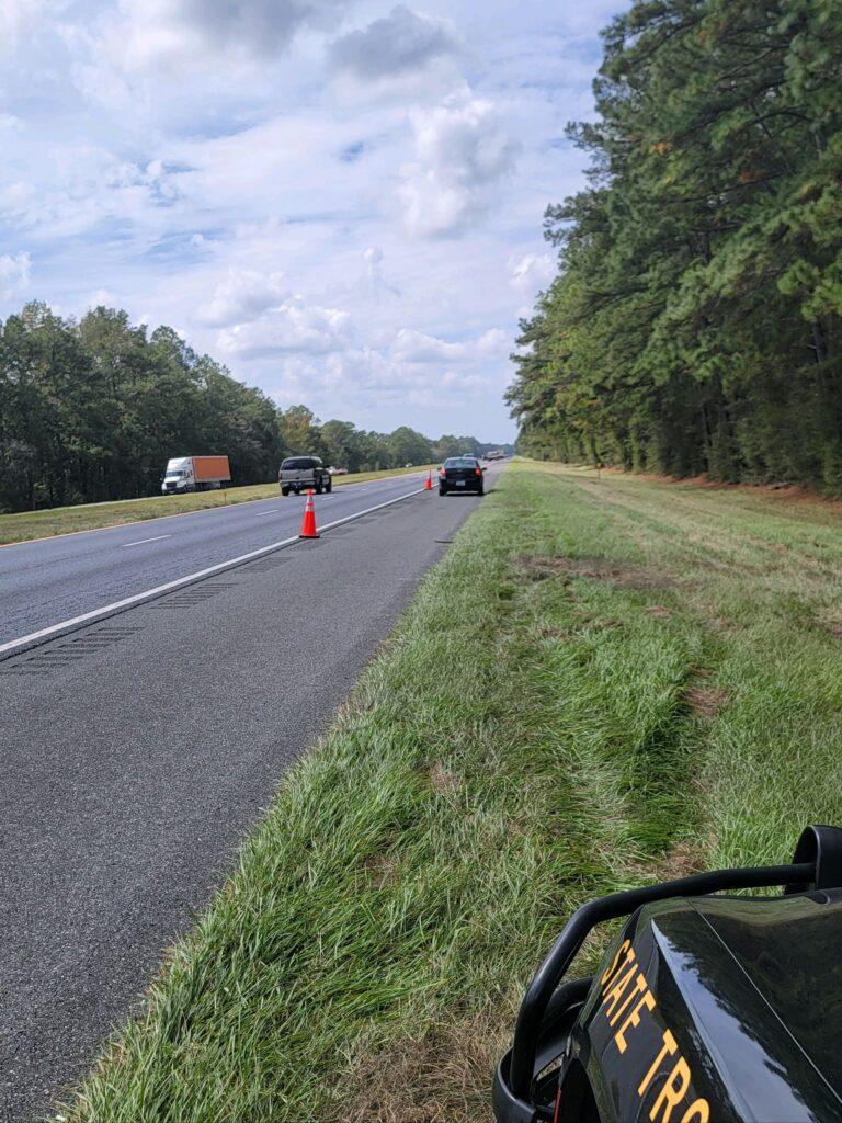 A car is driving down the road on a sunny day.