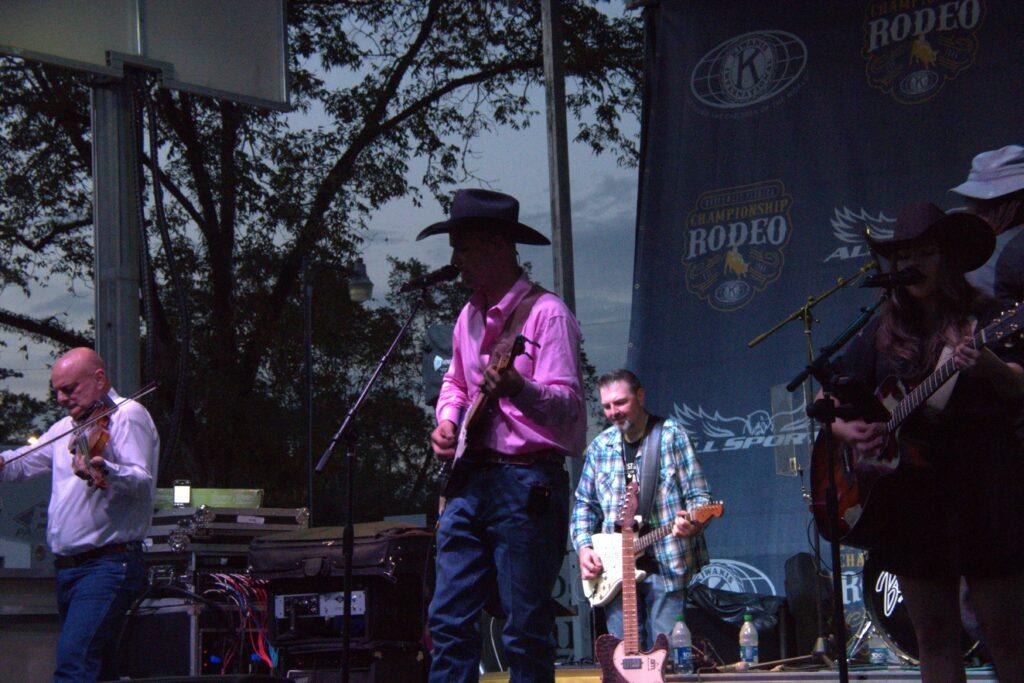 A man in cowboy hat and pink shirt playing guitar.