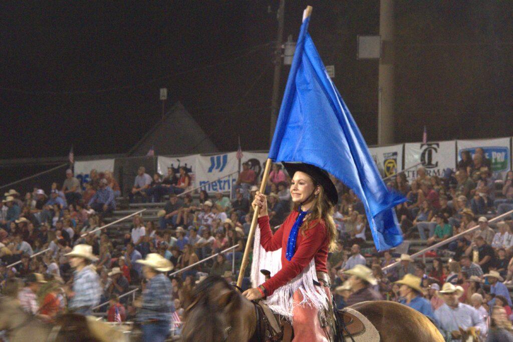 A woman holding a flag while riding on the back of a horse.
