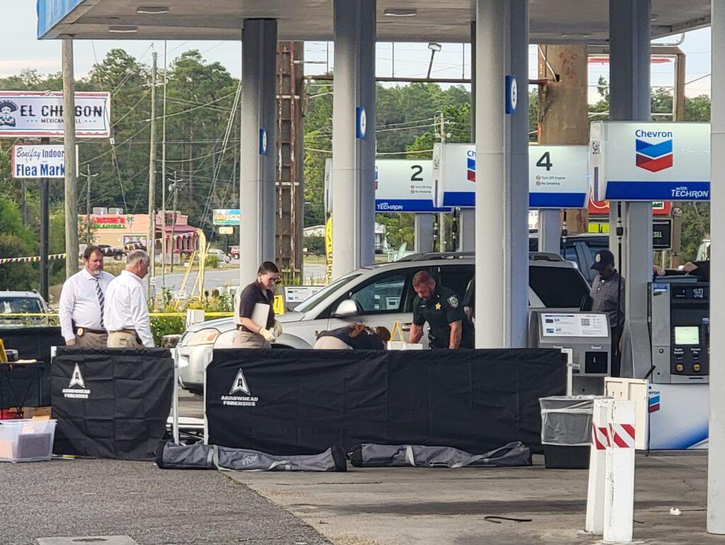 A group of people standing around cars at an outdoor gas station.