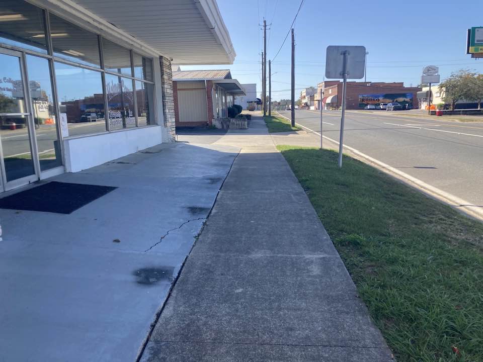 A sidewalk with grass and a building in the background.