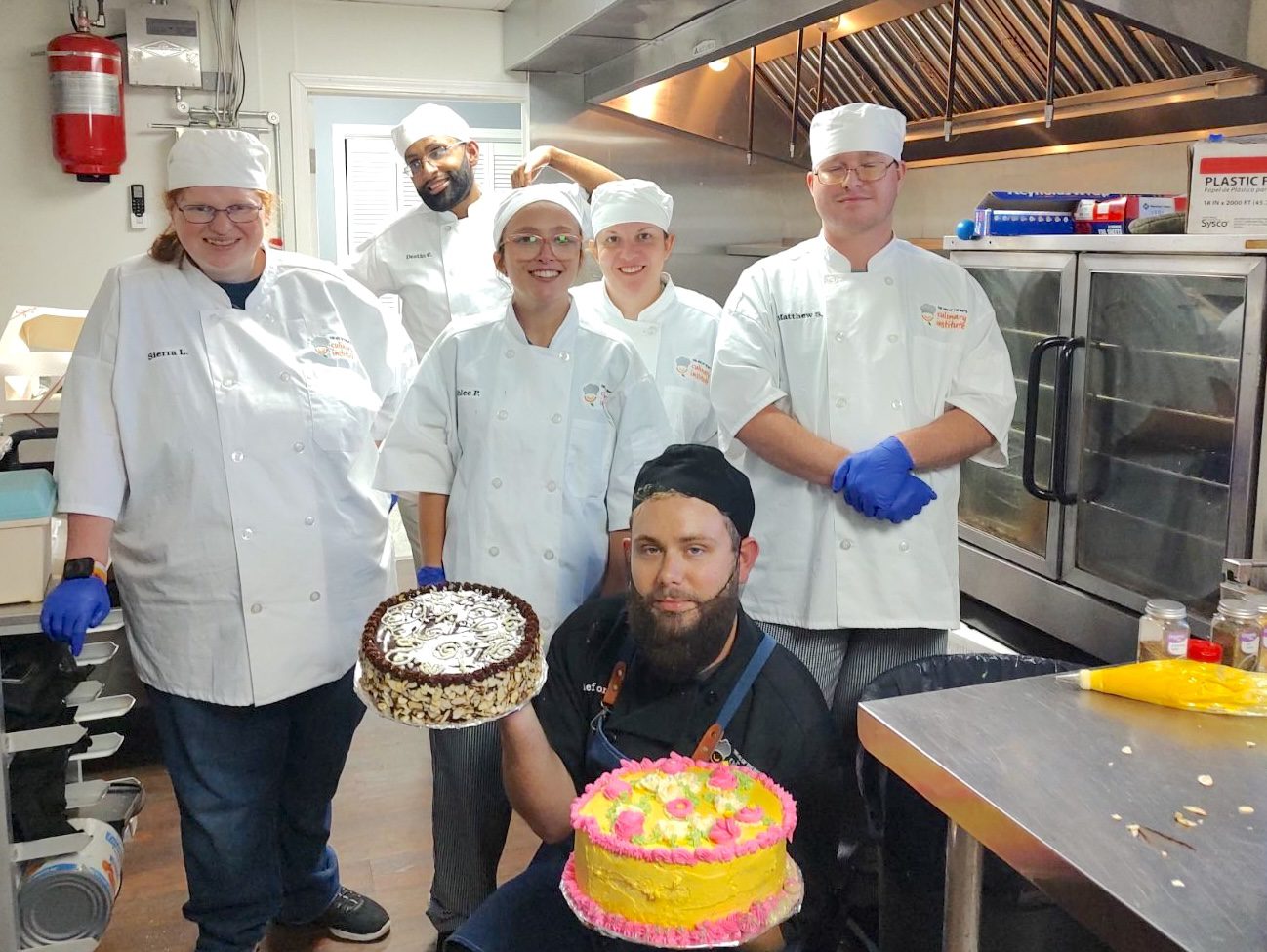 A group of people in a kitchen holding cakes to benefit local nonprofits