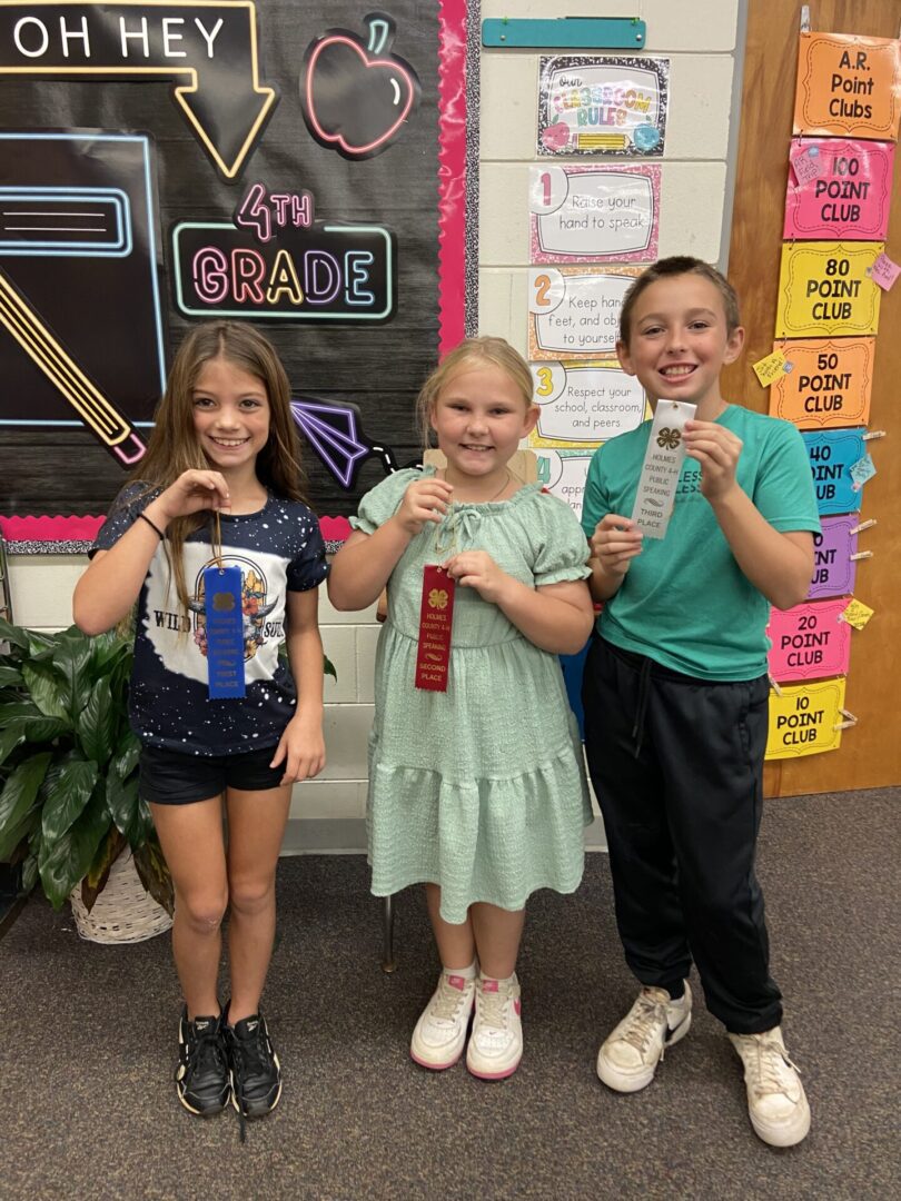 Three fourth-grade students holding award ribbons Three fourth-grade students holding award ribbons