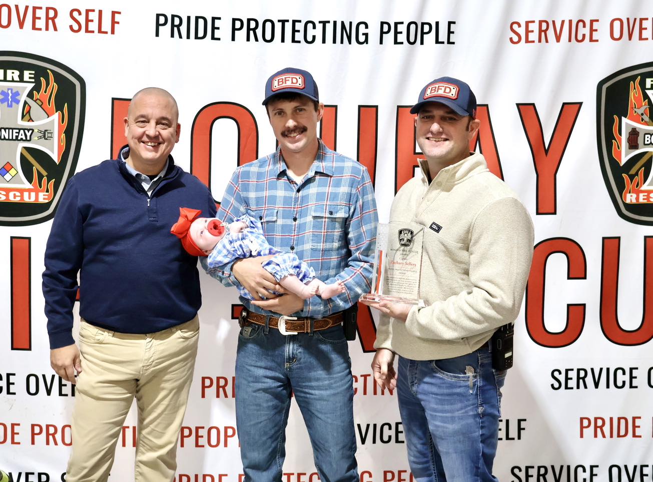 Firefighters holding infant training mannequin and trophy