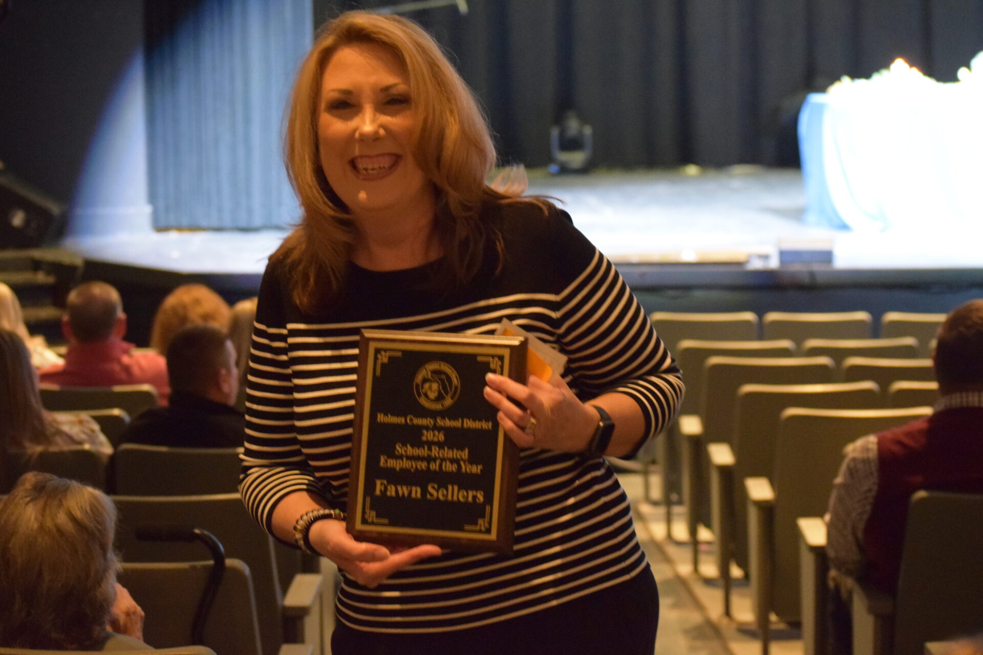 Smiling woman holding award plaque in auditorium